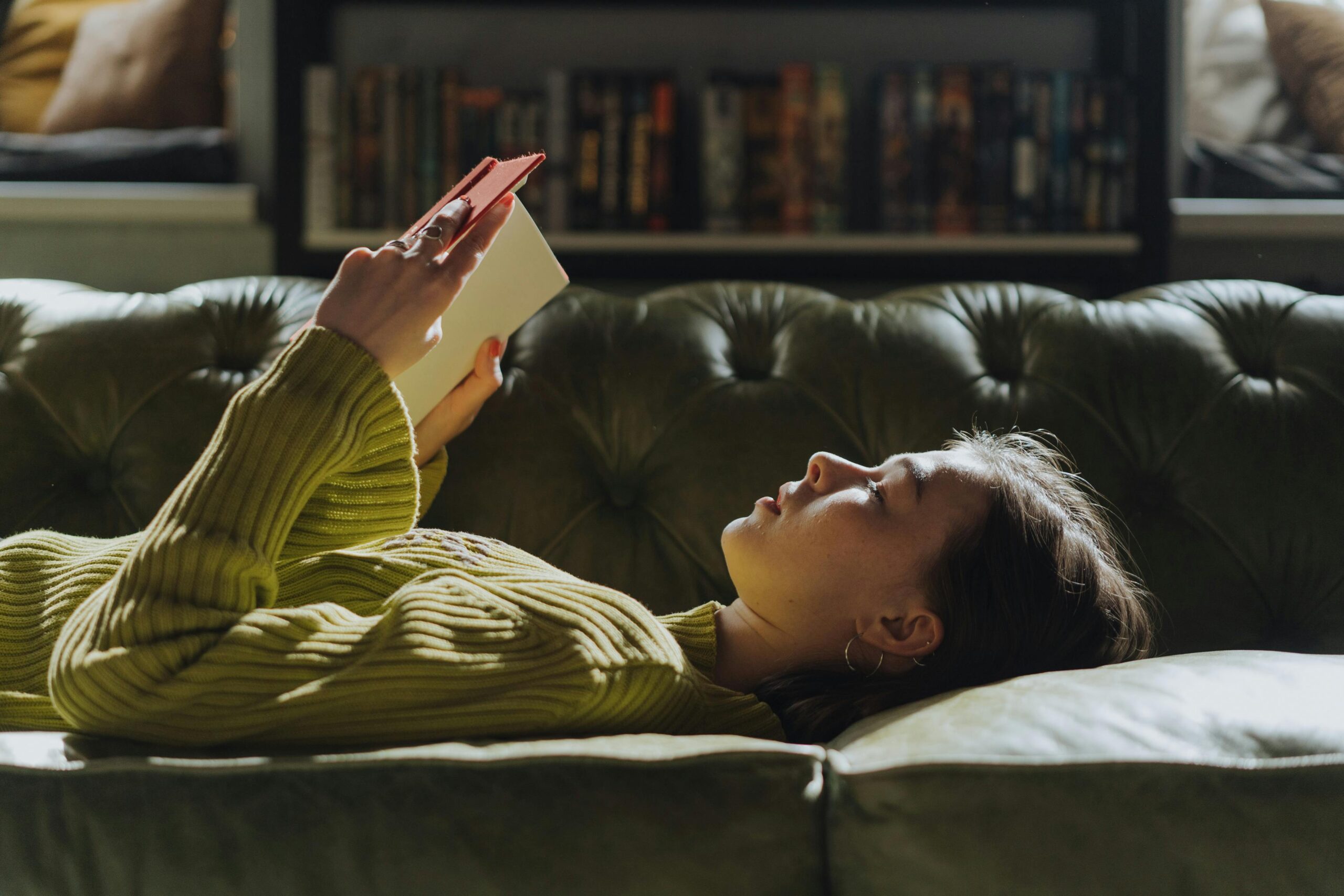 Image of a woman laying down on the sofa reading a book